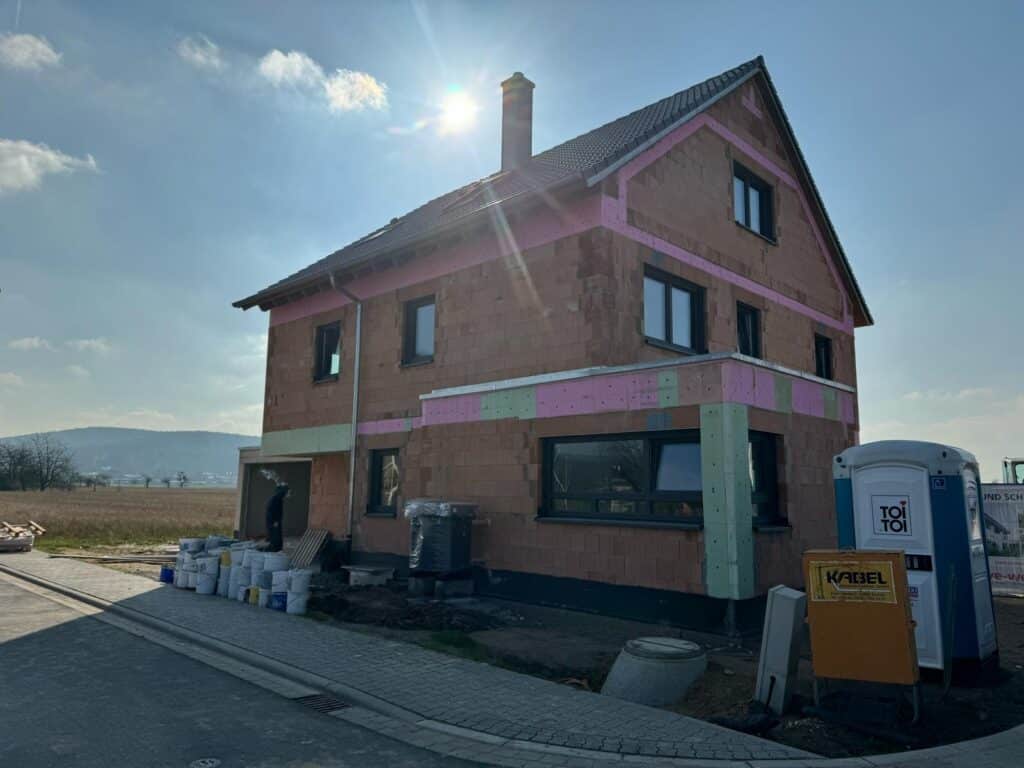 Ziegelrohbau mit eingesetzten Fenstern; Dach fertig, Sonne im Bild.