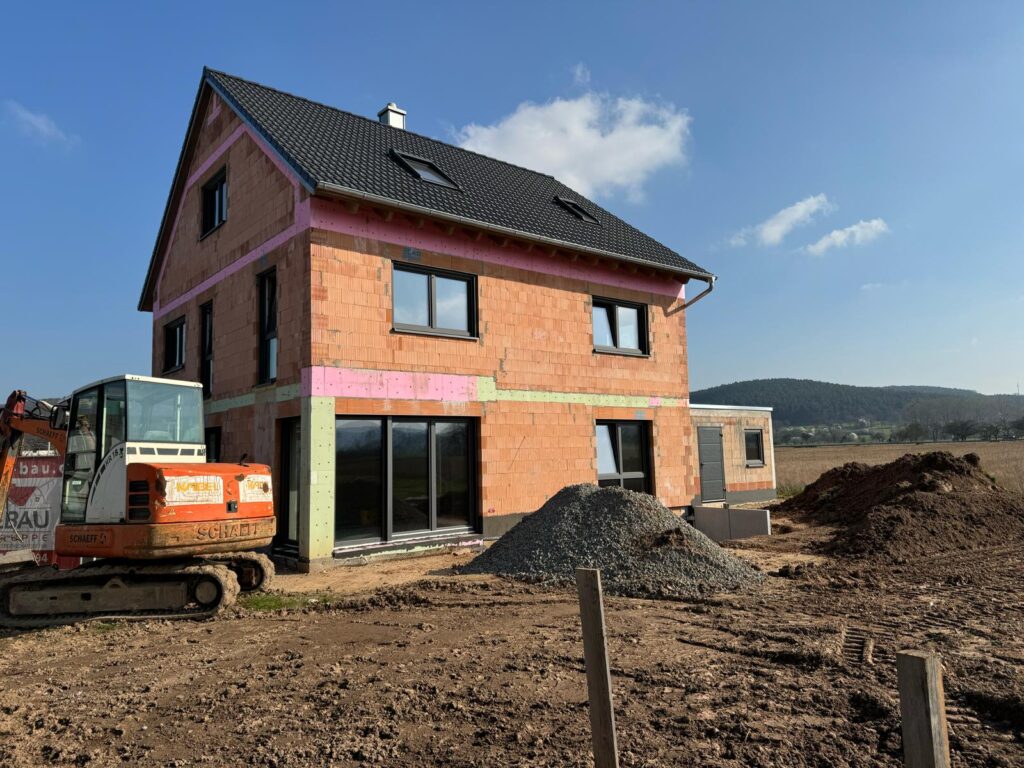Rohbau mit großen Schiebetüren; Erdarbeiten im Vorgarten.