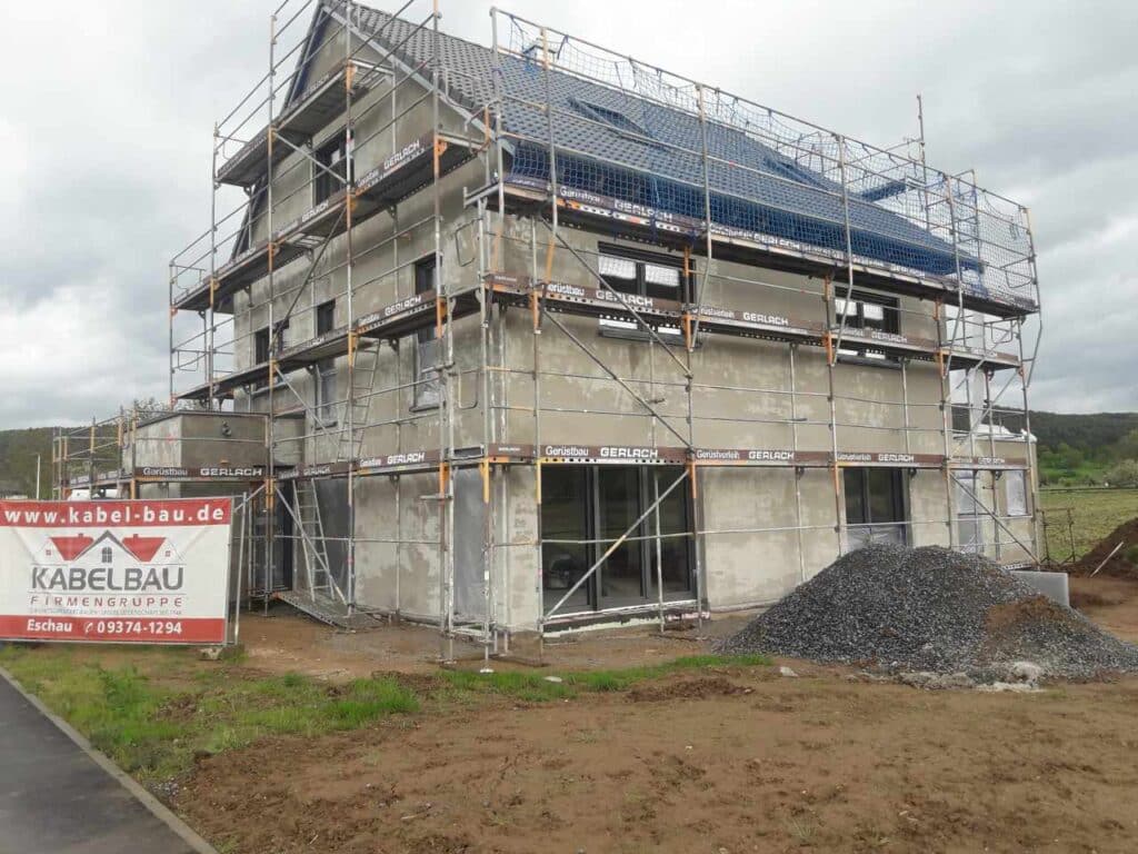 Seitenansicht des verputzten Hauses, Gerüst und Baustromkasten.