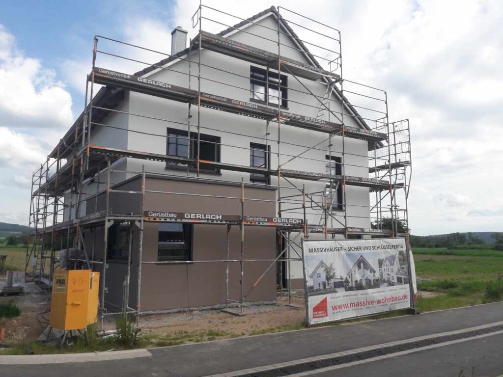 Zweifarbige Putzfassade (weiß/braun) mit Gerüst, Dach fertig gedeckt.
