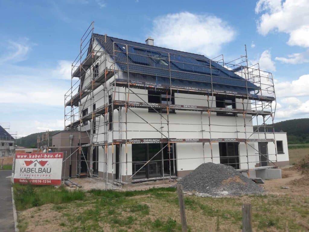 Rückansicht: weiß-braun verputztes Haus mit Gerüst und Ziegeldach.