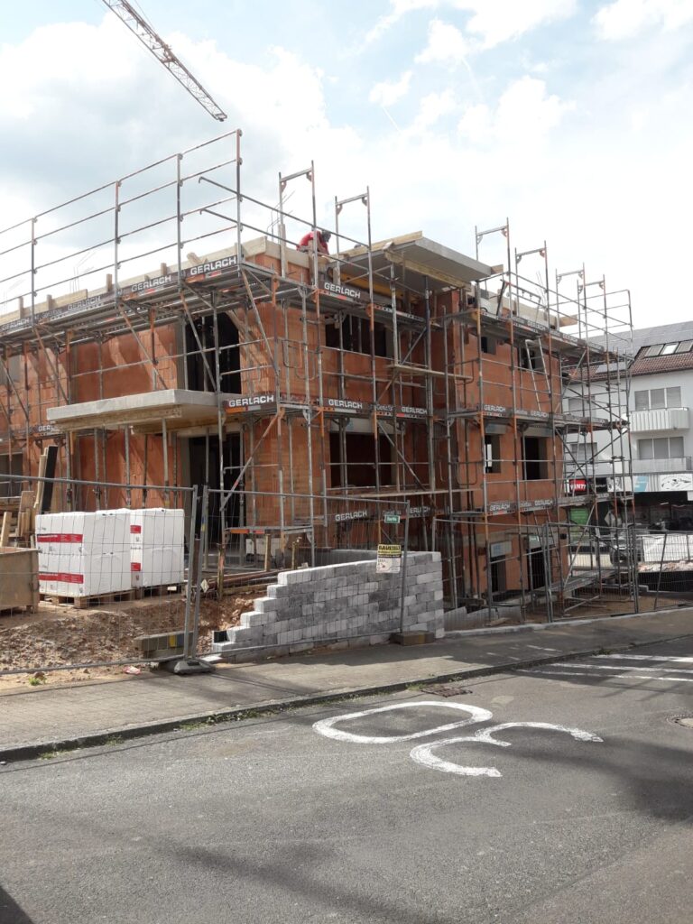 Ziegelrohbau-Ecke mit Gerüst; Deckenauflager und Öffnungen sichtbar.