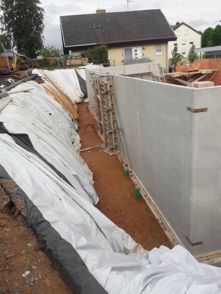 Weiße Abdichtung und Drainage an Kellerwand entlang der Baugrube.