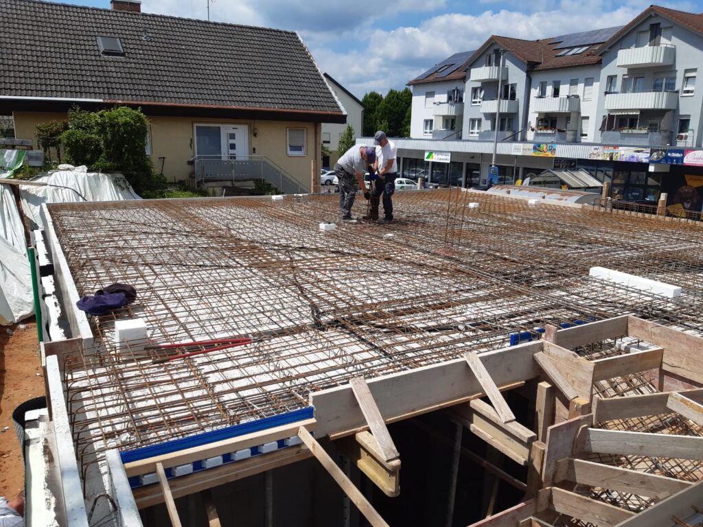 Arbeiter binden Bewehrungsmatte auf vorbereiteter Bodenplatte.