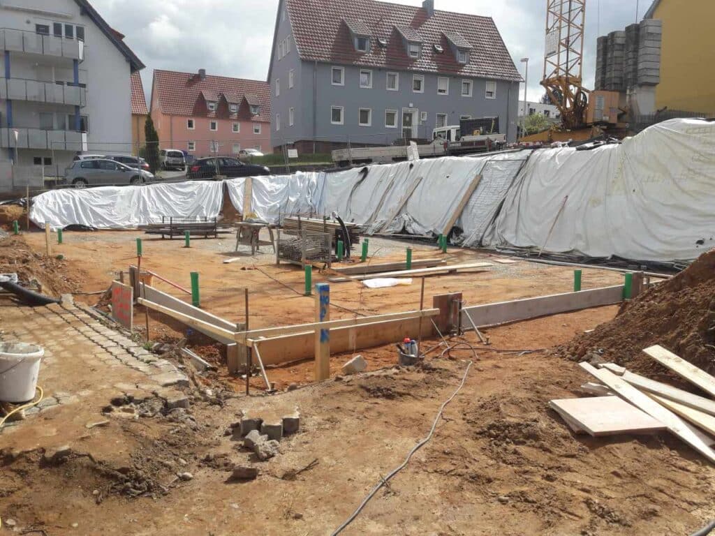 Holzschalungen für Streifenfundamente; Baugrube mit weißer Witterungsabdeckung.
