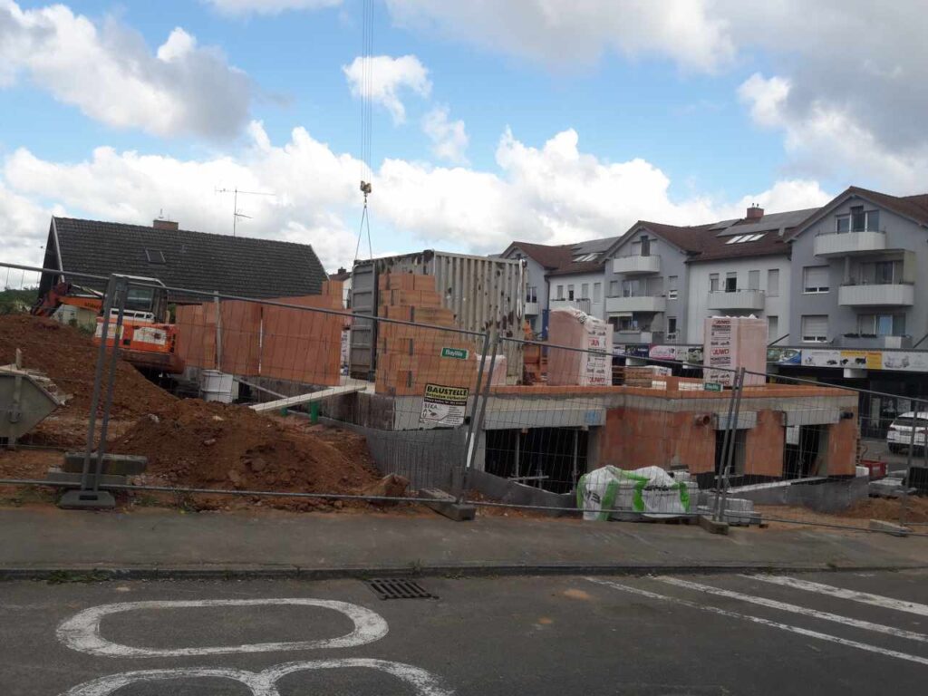 Straßenansicht: Erdgeschoss-Rohbau mit Materiallager.