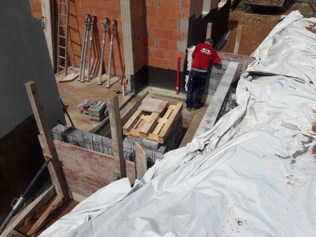 Abdichtungsarbeiten an Kelleraußenwand neben Baugrubenabdeckung.