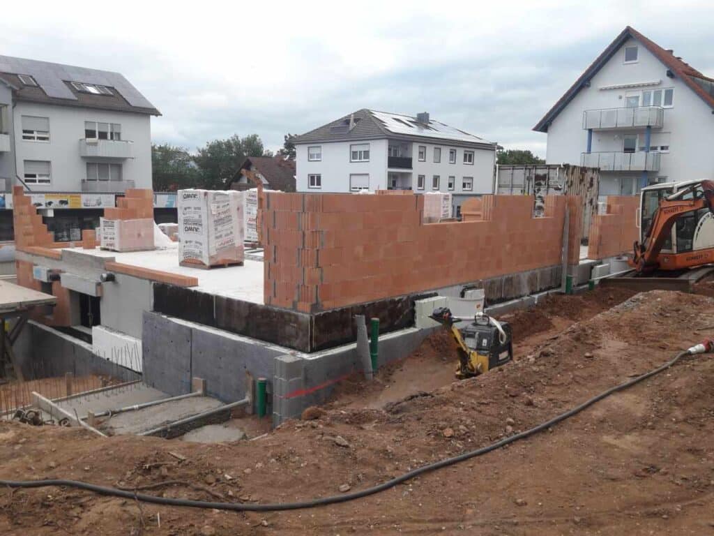 Überblick: Erdgeschoss-Mauerwerk wächst, Baumaschine vor Ort.
