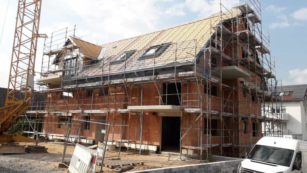 Eckansicht: Ziegelrohbau mit ausgebautem Dachstuhl und Gerüst.