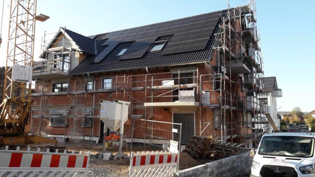 Mehrfamilienhaus im Rohbau, dunkles Dach, Gerüst ringsum.